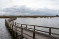 Long wooden pier and boardwalk in brackish water wetlands with esparto grass and lagoon under an overcast sky