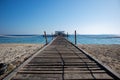 Long wooden pier (bridge) extents from beach to turquoise wave sea. Royalty Free Stock Photo