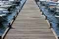 Long wooden pier with dense iron mooring bollards on each side and multiple small boats tied with strong ropes and chains