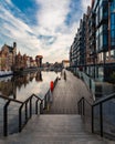 Long wooden platform next to long passage of buildings next to river with reflections of