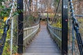 A long wooden suspension bridge over a river covered in fallen autumn leaves surrounded by lush green and autumn colored trees Royalty Free Stock Photo