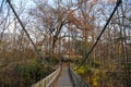 A long wooden suspension bridge over a river covered in fallen autumn leaves surrounded by lush green and autumn colored trees Royalty Free Stock Photo