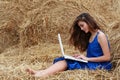 Longer-haired girl sitting on hay with laptop Royalty Free Stock Photo