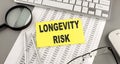 LONGEVITY RISK text written on a sticky on chart with keyboard and magnifier