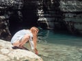 Longhaired girl washes her hands in clear turquoise river water while squatting on the bank in the canyon gorge