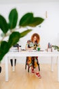 Longshot of a focused artist woman painting behind work desk shot through plant Royalty Free Stock Photo