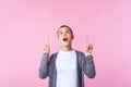 Look above! Portrait of amazed brunette teen girl standing with open mouth in surprise, pointing up at copy space. pink background