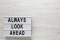 `Always look ahead` words on a lightbox, clipboard with blank sheet of paper on a white wooden surface, top view. Overhead, from Royalty Free Stock Photo