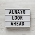 `Always look ahead` words on a modern board, clipboard with blank sheet of paper on a white wooden background, top view. Overhea