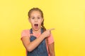 Look, crazy advertise! Portrait of amazed cute little girl in denim overalls pointing to side copy space Royalty Free Stock Photo