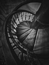 A look down to an old spiral staircase. Wooden circular stairway with ornate metallic railing, black and white vertical shot, Royalty Free Stock Photo
