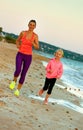 Smiling fit mother and child on seacoast in evening running