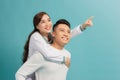 Look Here. Vertical portrait of happy couple pointing finger at side, man giving his lady piggyback ride