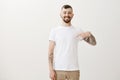 Look how clean my t-shirt. Portrait of satisfied good-looking pleased male with beard and tattos, pointing at chest and