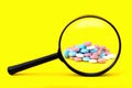 A look through a magnifying glass at a pile of pills on a yellow background. Search the ingredients of medicines, vitamins