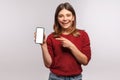 Look at mobile advertisement! Happy smiling brunette woman in shaggy sweater pointing cell phone with blank display