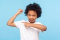 Look at my muscle, I`m strong. Portrait of adorable little boy in T-shirt pointing at biceps, feeling powerful and self-confident