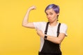 Look at my strength! Portrait of nice proud hipster girl pointing at biceps, feeling power and confidence. isolated on yellow