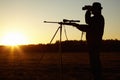 On the look out. A silhouette of a man in the wildlife with his sniper rifle ready and looking through his binoculars.