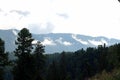 A look through the tall pines to the tops of the mountains overgrown with coniferous forests lying under a blue cloudy sky