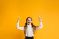 Excited School Girl Pointing Fingers Up Over Yellow Background, Copyspace