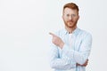 Look there now. Portrait of handsome redhead male with beard in eyewear and shirt pointing at upper left corner and