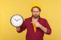 Look at time! Portrait of impatient angry hipster guy in checkered shirt pointing big clock and looking displeased Royalty Free Stock Photo