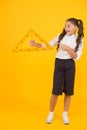 Look at the triangle with two equal sides. Happy little schoolgirl holding triangle on yellow background. Cute small kid