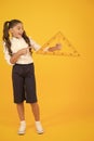 Look at the triangle with two equal sides. Happy little schoolgirl holding triangle on yellow background. Cute small kid