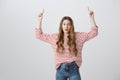 Look up if your are brave. Studio shot of scared stunned cute teenage girl with blonde hair raising hands and pointing