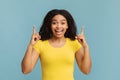 Look upward. Overjoyed african american woman pointing fingers up, looking and smiling to camera on blue background Royalty Free Stock Photo