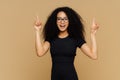 Look upwards. Happy African American woman points above with both index fingers, has slim figure, wears black t shirt, promots Royalty Free Stock Photo