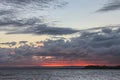 Looking across the water at sunset with dark storm clouds lit up from underneath by a blood red sun sinking behind distant Royalty Free Stock Photo