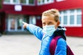 Looking aside Attractive schoolboy in protective mask standing outdoor excited child points finger at school close up Royalty Free Stock Photo