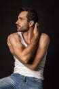 Portrait of young handsome bearded sad man in white undershirt and jeans looking away isolated on dark background Royalty Free Stock Photo