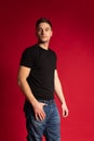 Portrait of young handsome sportive man in black t-shirt and blue jeans posing isolated on red studio background. Royalty Free Stock Photo