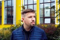 Looking away young caucasian 34 years old man in blue jacket with goatee beard on yellow facade of college modern building. Young