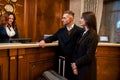 Looking for the best option. Happy couple checking in hotel at reception desk. Man and woman with a suitcase waiting for Royalty Free Stock Photo