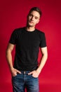 Portrait of young handsome sportive man in black t-shirt and blue jeans posing isolated on red studio background. Royalty Free Stock Photo