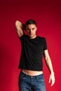 Portrait of young handsome sportive man in black t-shirt and blue jeans posing isolated on red studio background. Royalty Free Stock Photo