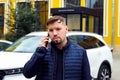 Looking at camera Young Caucasian 34 years old sad concentrated man with goatee beard talks on smartphone on street near white car Royalty Free Stock Photo