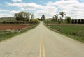 Looking down middle of the road in Shell, Wyoming, you see pasture land, trees and farm houses with blue sky.