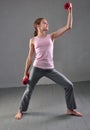 Looking down teenage sportive girl is doing exercises to develop with dumbbells muscles on grey background. Sport healthy