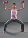 Looking down teenage sportive girl is doing exercises to develop with dumbbells muscles isolated on grey background. Sport healthy