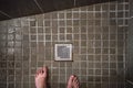Looking down to hotel room shower drain grid, wet tiles on floor, man feet visible in lower part