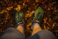 Looking down towards the ground with feet in sport shoes firmly standing on the ground covered with brown autumn leaves