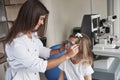 Looking at each other. Little girl tries new blue glasses in ophthalmologic office with female doctor