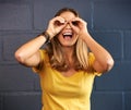 Looking at the funny side of life. a young woman looking through her fingers against a brick wall background.