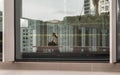 Looking through glass wall saw a young asia woman sitting on Modern wood bench in Lobby room. She is view smart phone messages