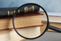 Looking through magnifying glass at stack of vintage books on table, closeup. Search concept